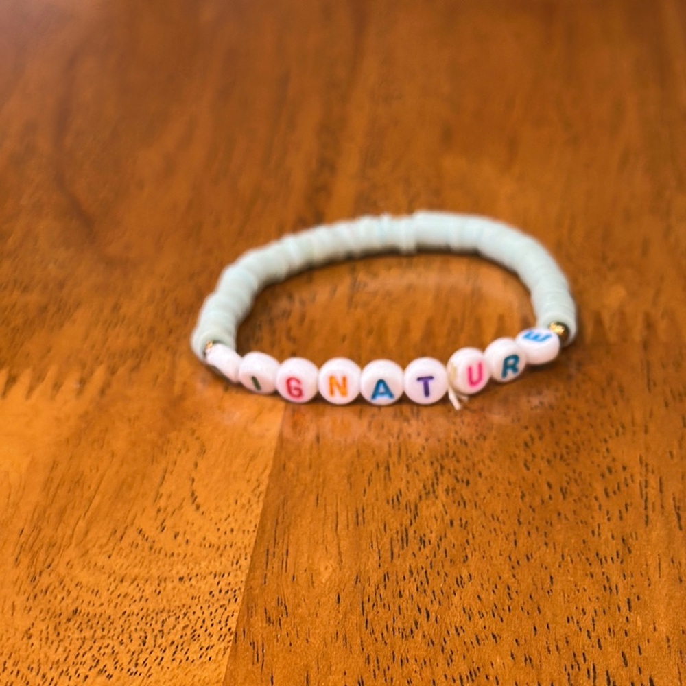 Kids shell bracelet with the word “signature”. Light teal shells.